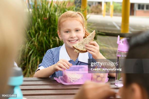 young girl with red hair eating sandwich on school lunch break - healthy eating children stock pictures, royalty-free photos & images