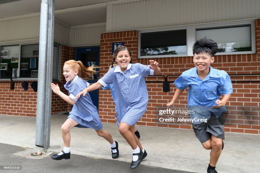 Three children running out from school across playground laughing