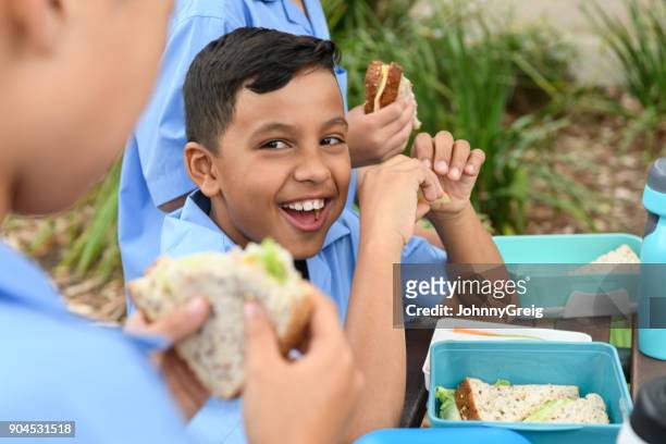 etnische jongen eten lunchpakket kant met schoolvrienden - boy in a box stockfoto's en -beelden