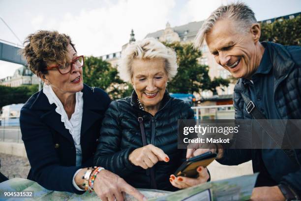 senior male and female friends with map and mobile phone in city - stockholm map stock pictures, royalty-free photos & images