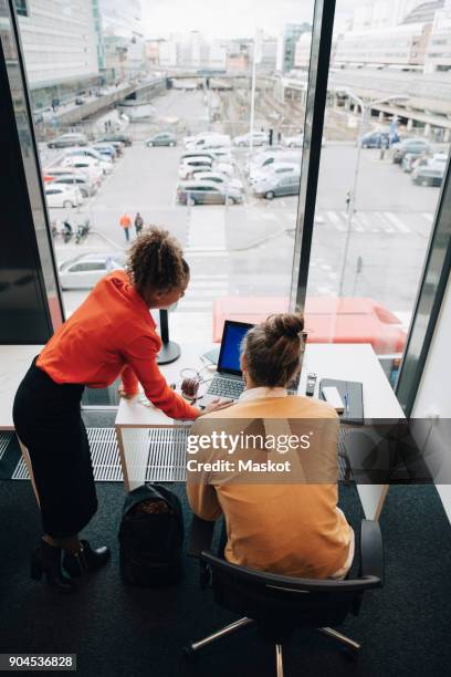 high angle view of multi-ethnic colleagues using laptop at desk in office - man leaning chair standing side view stock pictures, royalty-free photos & images