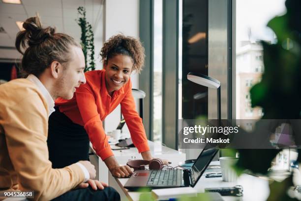 smiling businesswoman leaning on desk while looking at businessman sitting at office - desktop picture stock pictures, royalty-free photos & images