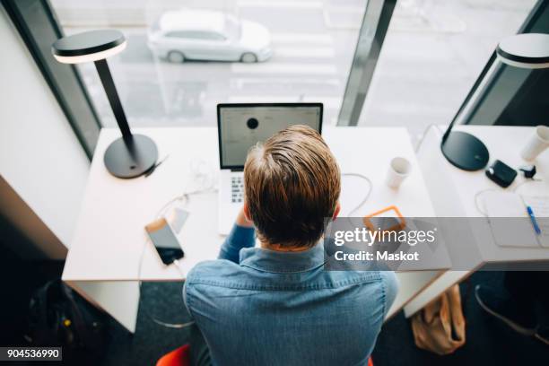 high angle rear view of businessman working at desk in office - working behind laptop fotografías e imágenes de stock