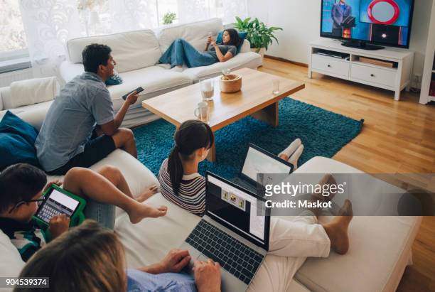 high angle view of family using technologies while relaxing in living room at home - equipment stock pictures, royalty-free photos & images