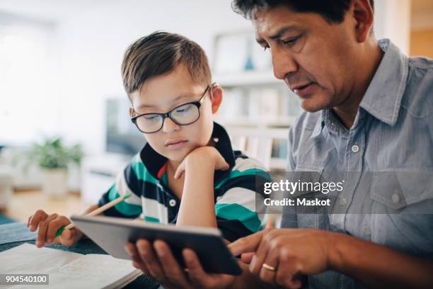 father showing digital tablet to son while studying at table - disabilitycollection fotografías e imágenes de stock