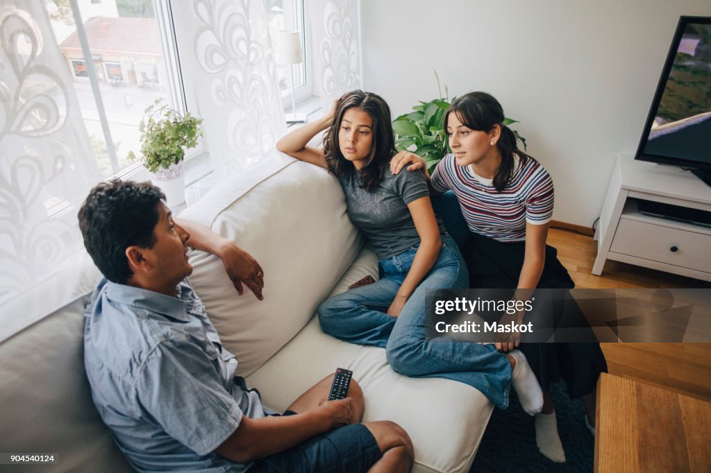 Daughters listening to father while sitting on sofa at home