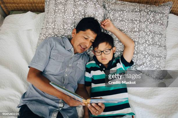 High angle view of father reading book to son while lying on bed at home