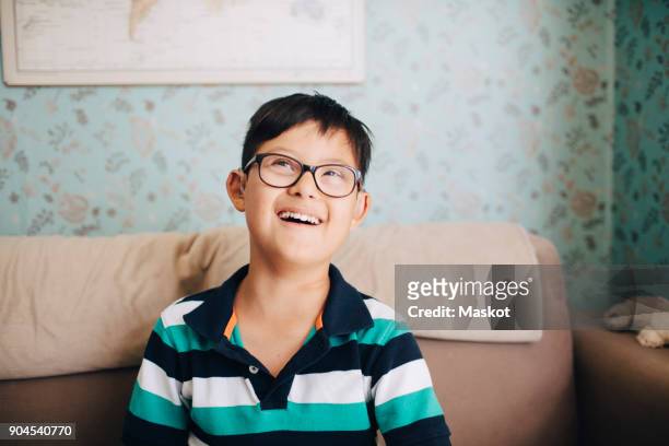 Thoughtful disabled boy laughing while sitting on sofa at home