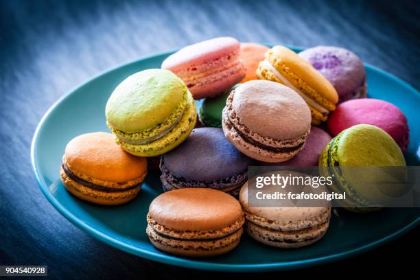 multi colored macaroons in a blue plate shot on blue table - macaron stock pictures, royalty-free photos & images