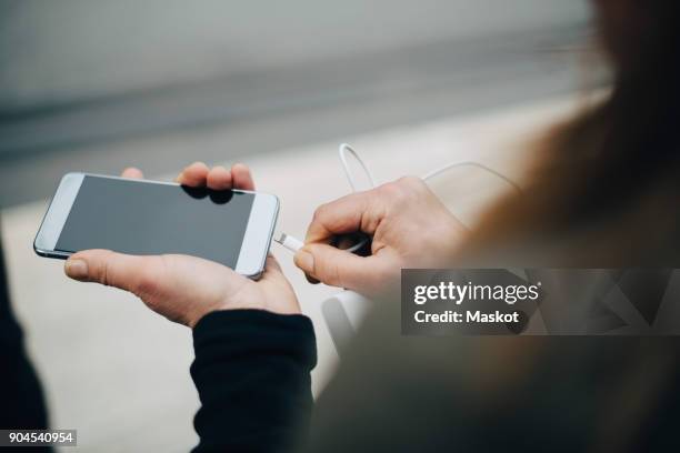 cropped image of mature businesswoman inserting usb cable in smart phone - charging phone stock-fotos und bilder