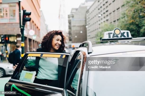 smiling mid adult businesswoman entering taxi on street in city - taxi van stockfoto's en -beelden