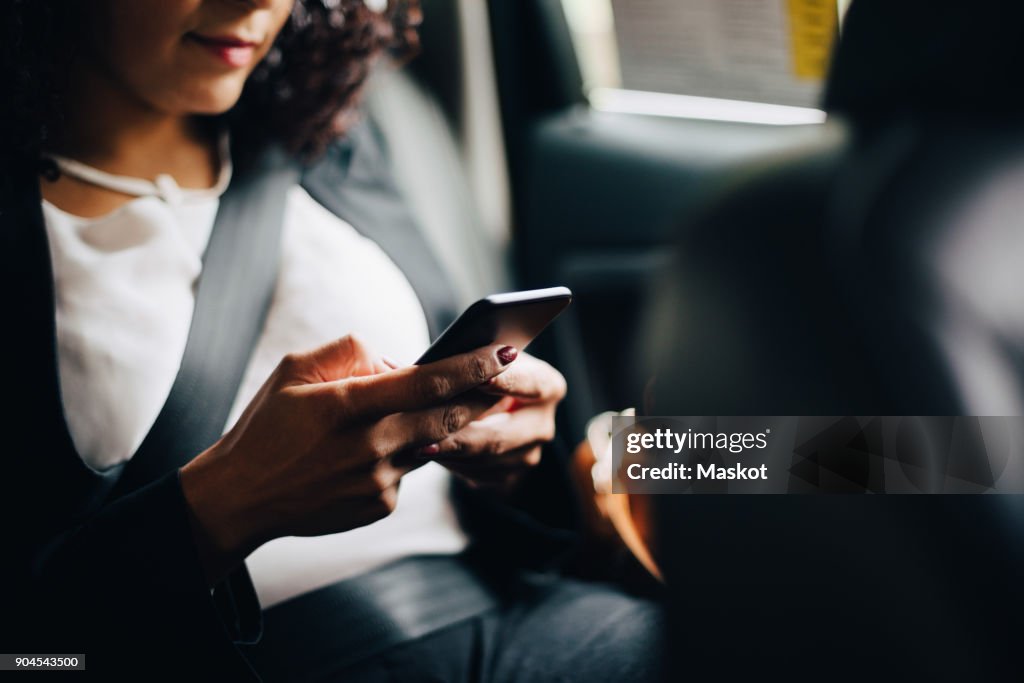 Midsection of businesswoman using smart phone while sitting in taxi