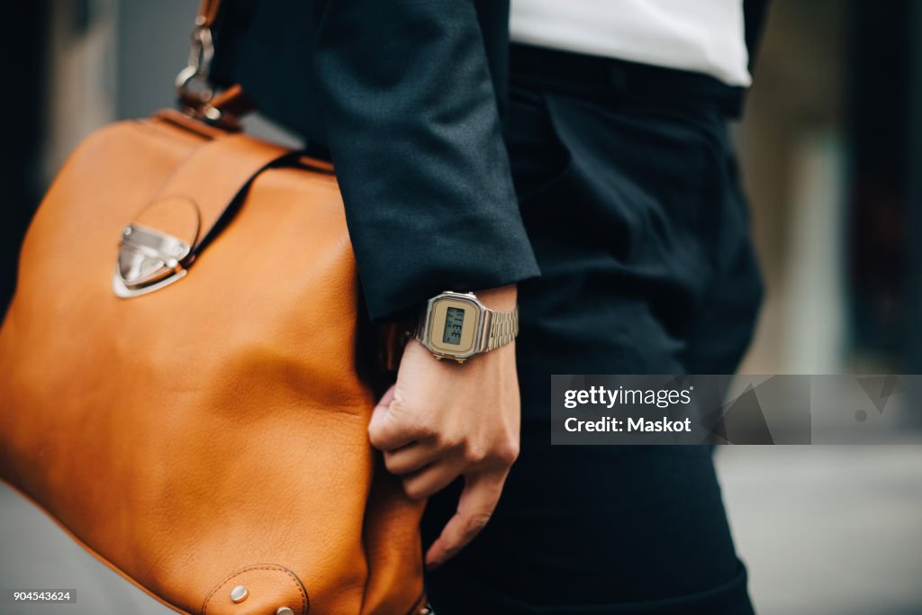 Midsection of businesswoman with orange purse standing in city