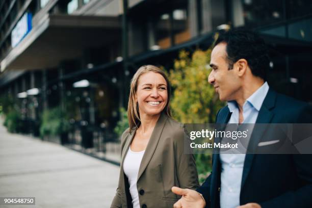 smiling mature business colleagues talking while walking in city - business outdoor stockfoto's en -beelden