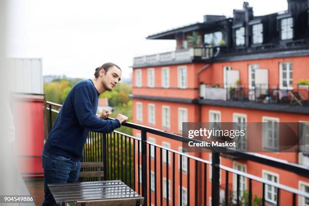young man standing in balcony at urban rental apartment - apartment exterior ストックフォトと画像