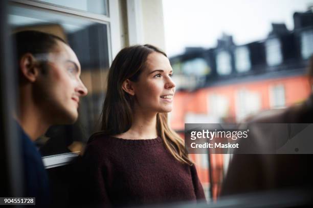 smiling woman with friends looking away while standing in balcony of rental apartment - looking away stock-fotos und bilder