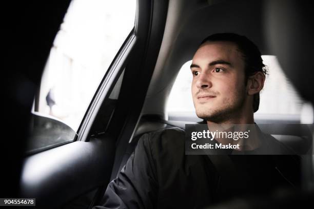 thoughtful young man looking through window while riding in car at city - looking out car window stock pictures, royalty-free photos & images