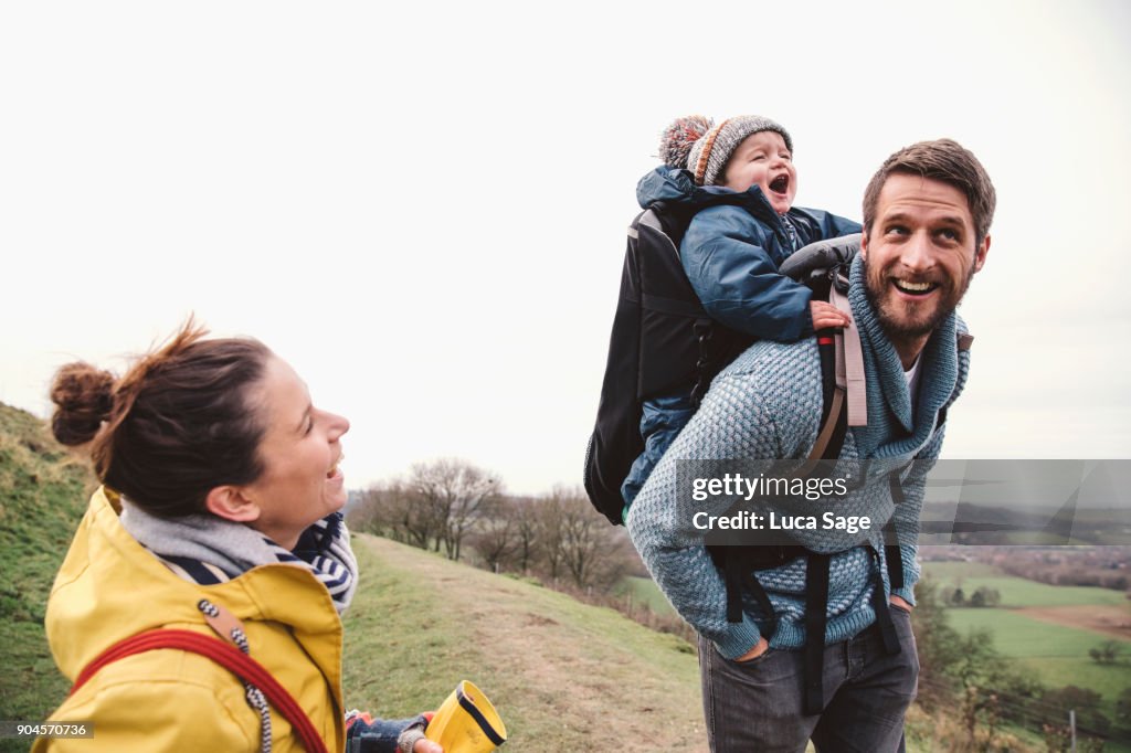 A mother and father with their son on the fathers back, whilst walking in the countryside