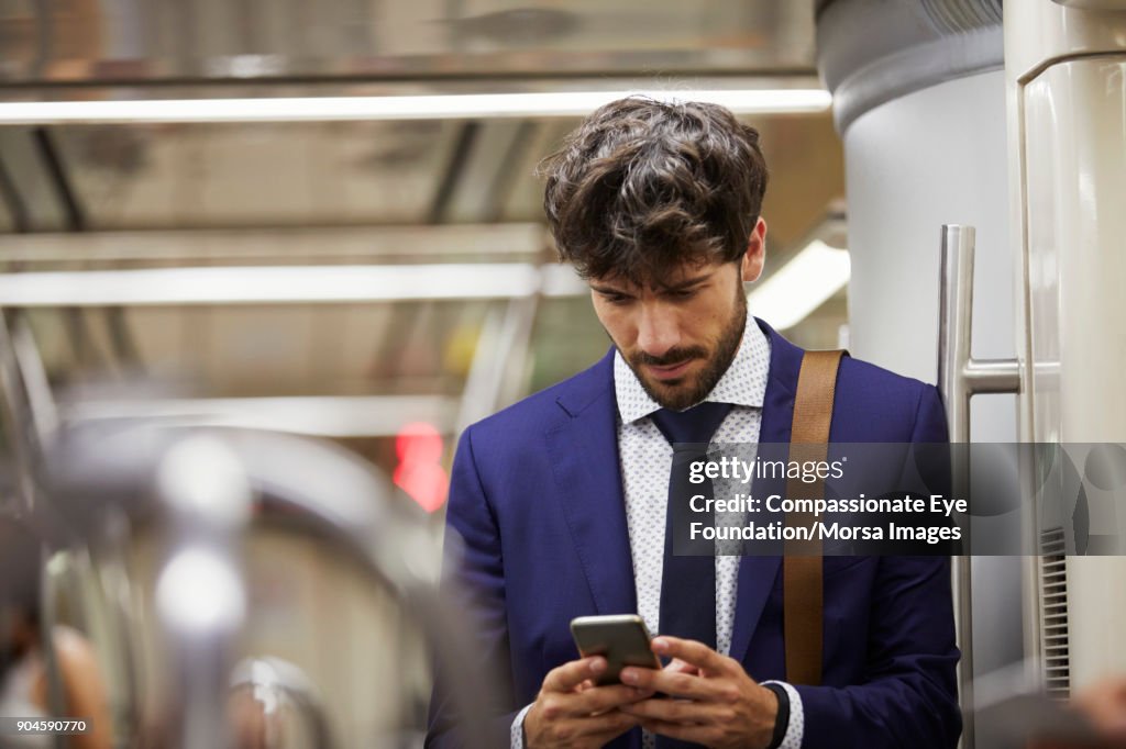 Businessman using cell phone on subway train