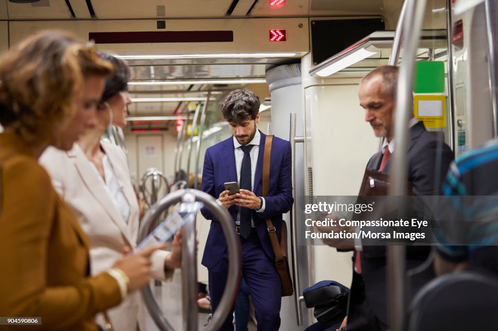 Businessman using cell phone on subway train