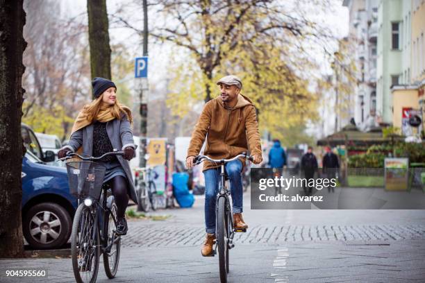 smiling friends cycling on city street in winter - two cars side by side stock pictures, royalty-free photos & images