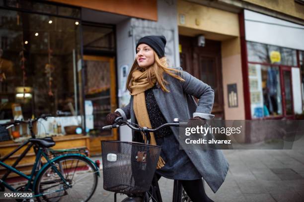 smiling young woman riding bicycle by building - woman jacket stock pictures, royalty-free photos & images