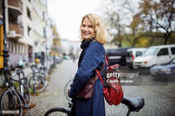 lächelnde frau mit dem fahrrad in die stadt im winter - leben in der stadt stock-fotos und bilder