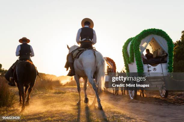 group of people in horse-drawn wagons and on horseback on a rural dusty road. - andalucia stock pictures, royalty-free photos & images