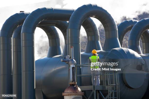 rear view of woman engineer standing on a platform at a geothermal plant. - geothermische centrale stockfoto's en -beelden