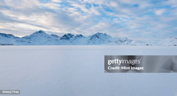 winter landscape under a cloudy sky, with mountains in the distance. - artic stock-fotos und bilder