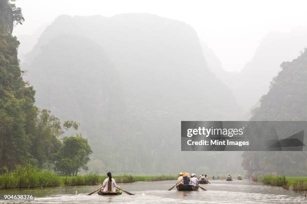 groups of people in rowboats on a river, mountains in the background. - vietnamese mint stock pictures, royalty-free photos & images