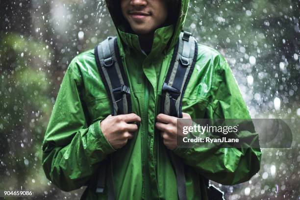 junger mann wandern im regen mit wasserdichte jacke - raincoat stock-fotos und bilder