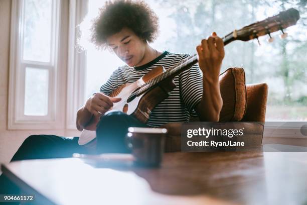 joven tocando la guitarra en living home - cantautor fotografías e imágenes de stock