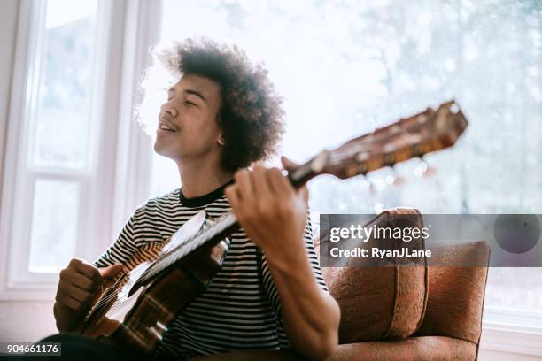 joven tocando la guitarra en living home - cantautor fotografías e imágenes de stock