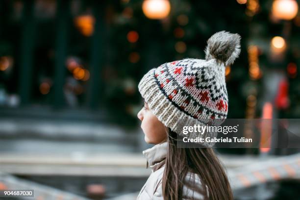 a girl wearing a cute woolly hat enjoys the view of the christmas lights - navidad ストックフォトと画像