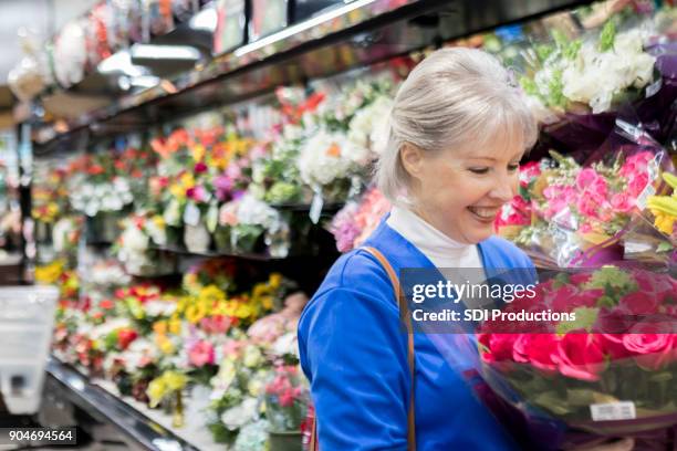 senior woman inspects bouquet of roses in grocery store - coronal section stock pictures, royalty-free photos & images