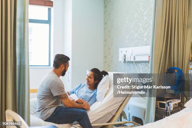 man sitting with ill female patient on bed in ward - visit stock pictures, royalty-free photos & images