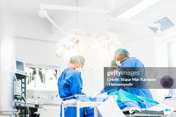 chirurgen die onder verlichtingsapparatuur - operation stockfoto's en -beelden