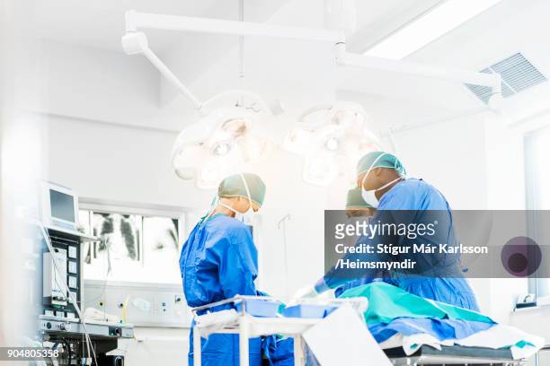 surgeons operating below lighting equipment - surgery stock pictures, royalty-free photos & images