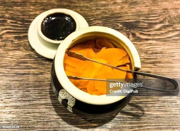 takuan served in small jar with stainless steel tongs on wood table - takuan stockfoto's en -beelden