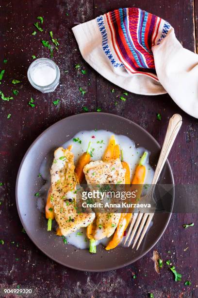 roasted white fish fillet with cream sauce and baby carrots on a plate, top view - sahnesoße stock-fotos und bilder