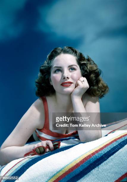 An unidentified model lies on a striped towel, a pair of red sunglasses in one hand, and gazes wistfully into the cloudy 'sky' of a photo studio,...