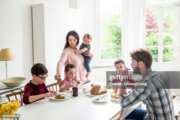 upptagen familj äter frukost, mor som serverar son toast samtidigt bär baby pojke - fyrbarnsfamilj bildbanksfoton och bilder