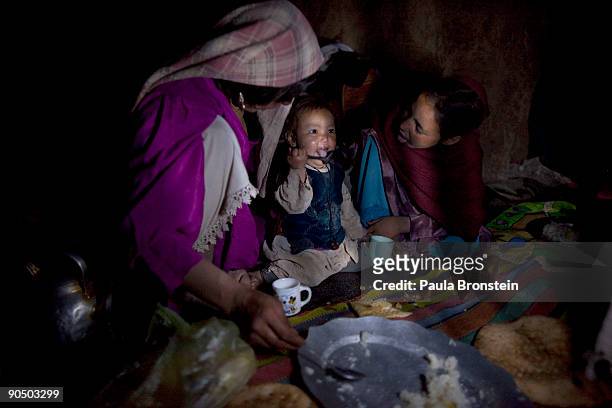 Anissa helps feed daughter Hadisha, 16 months, some rice for dinner as older sister Anifa looks on inside their cave September 7, 2009 in Bamiyan,...