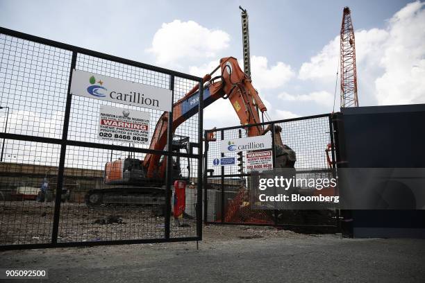 Digger operates near the gates of a construction site for new apartment blocks built by Carillion Plc in the Canning Town district of London, U.K.,...