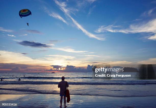 Beachgoer watches parasailing off the beach in Phuket. Tourists can take short parasailing flights from the beach out toward the small island, Koh...