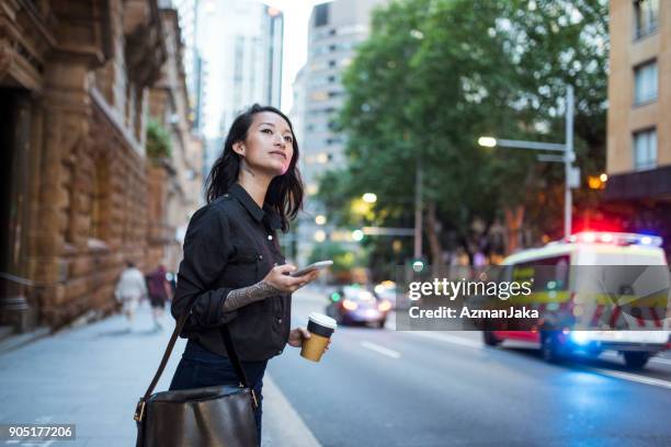 asian woman waiting for an uber and drinking coffee - traffic australia stock pictures, royalty-free photos & images