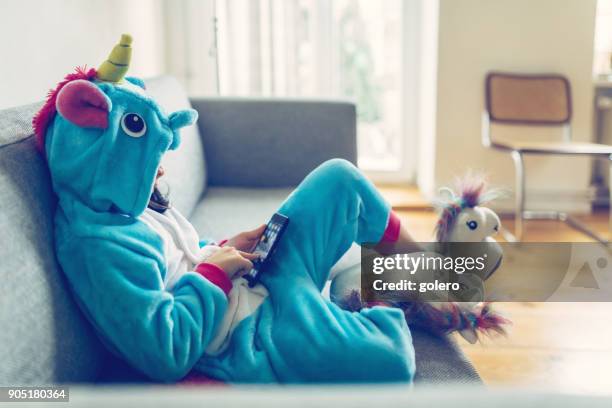 kleines mädchen mit einhorn kostüm mit mobile auf couch - kostüm stock-fotos und bilder