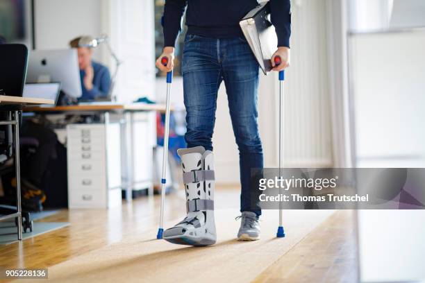Berlin, Germany Symbolic photo on the topic: Sick at work. A man walks through a office with crutches and an orthosis on his leg on January 15, 2018...