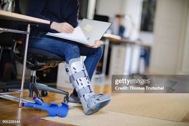 Berlin, Germany Symbolic photo on the topic: Sick at work. A man with crutches and an orthosis on his leg sitting at a desk in the office on January...